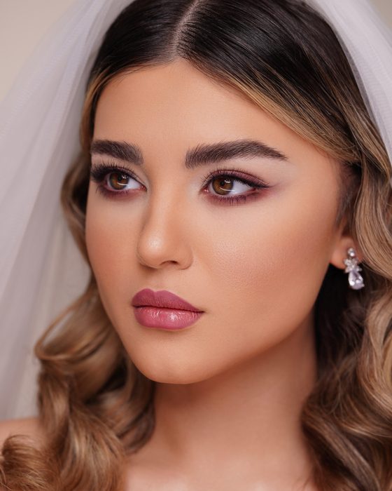 Kühle Pflaumen- und Mauve-Nuancen rahmen die Augen weich ein, während natürliche Nude-Lippen den Look klar, elegant und modern halten.