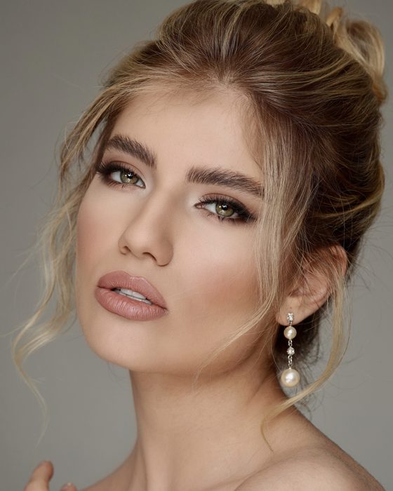 Moderner Nude-Bridal-Look mit weichen Brauntönen, gelifteter Augenform, dezenten Konturen und eleganten Perlenohrringen.