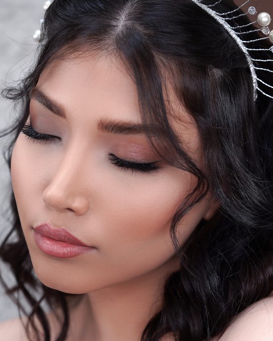 Moderner Bridal Look mit soften Mocha- und Taupe-Tönen, dunklen Wellen, glänzenden Nude-Lippen und außergewöhnlichem Perlenschmuck.