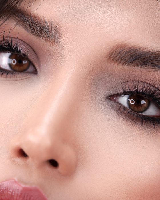 Moderner Bridal Look mit soften Mocha- und Taupe-Tönen, dunklen Wellen, glänzenden Nude-Lippen und außergewöhnlichem Perlenschmuck.