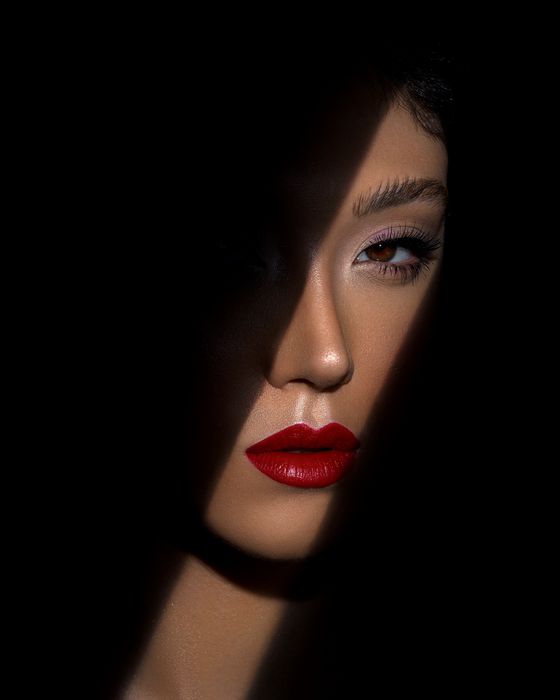 Editorial Beauty Look mit grafischer Lichtführung, präzisem Augen-Make-up und ausdrucksstarken roten Lippen.