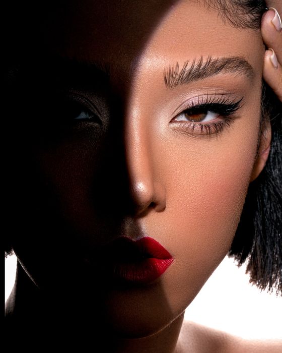 Editorial Beauty Look mit grafischer Lichtführung, präzisem Augen-Make-up und ausdrucksstarken roten Lippen.
