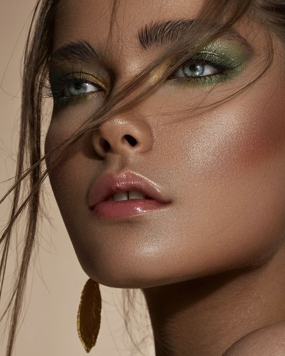 Editorial Make-up mit Smaragdgrün, Goldnuancen, strahlender Haut und glänzenden Nude-Lippen.